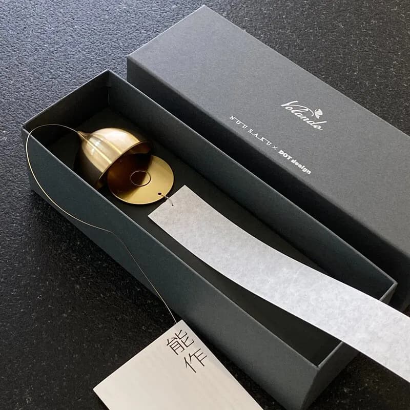 黑色盒裝打開展示金色圓形物件與白色長條紙材,盒蓋印有白色品牌字樣,旁邊放著能作卡片。