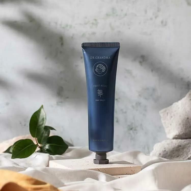 深藍色軟管直立於石板上,管身印有 DR.GRANDMA 標誌與 FOOT CREAM 字樣,旁有綠葉。