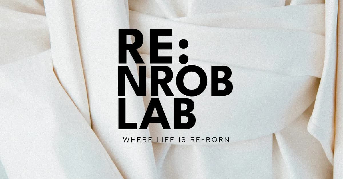 白色皺褶布料背景上印有黑色「RE:NROB LAB」標誌,下方寫著「WHERE LIFE IS RE-BORN」。