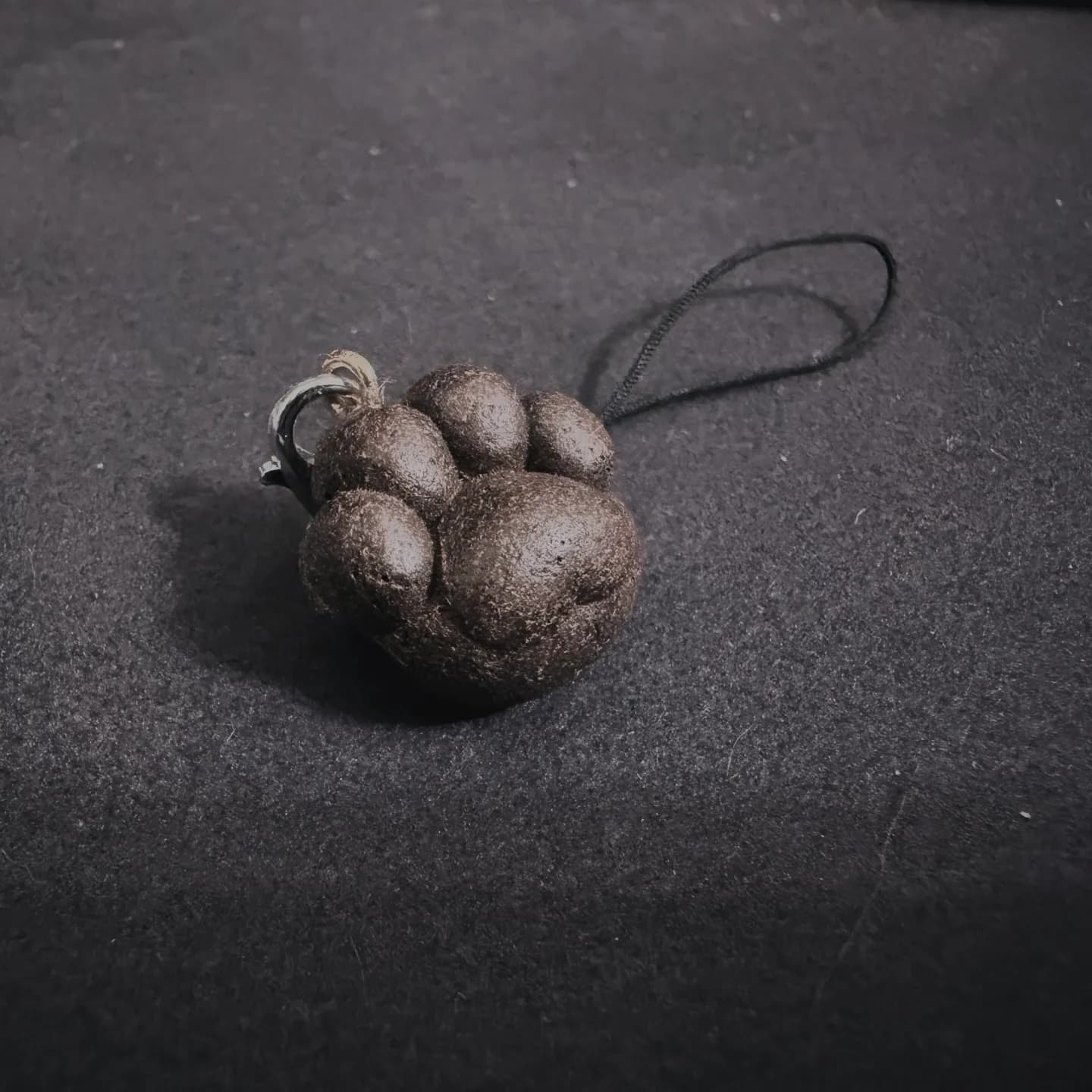 深褐色圓潤多瓣石雕吊飾置於黑色布面,後方連接黑色繩圈,表面帶有粗糙顆粒質感。