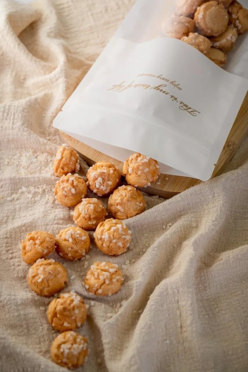 Golden-brown round pastries with a textured coating arranged on beige fabric beside a white paper package.