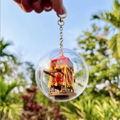 A handmade keychain from Simply Made, featuring a small red temple inside a transparent sphere, with green plants in the background.